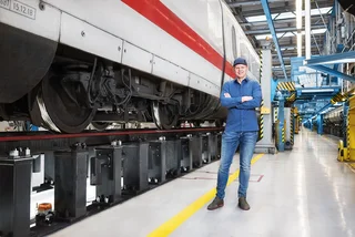 Ein Kunde steht vor einem ICE welcher auf aufgeständerten Gleisen steht. 