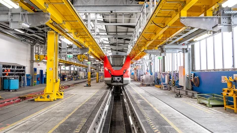 Dacharbeitsbühne Arbeitsplattform auf dem Dach eines Schienenfahrzeugs in einer Industriehalle, mit Geländern und Zugangstreppen für Wartungsarbeiten.